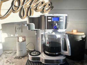 dual purpose single serve and full pot coffee maker on a kitchen counter with mug and plant